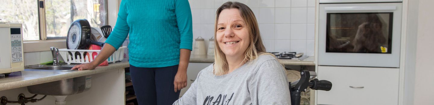 Adult preparing a fresh meal with a friendly support worker in a home kitchen